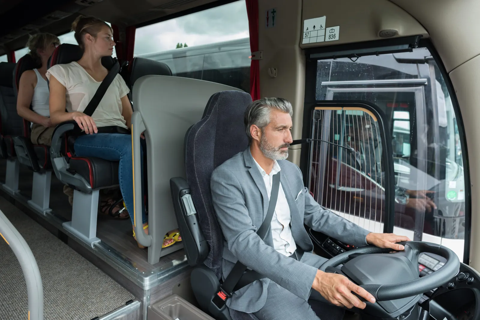 Bussjåfør med sikkerhetsbelte og passasjerer i setene bak