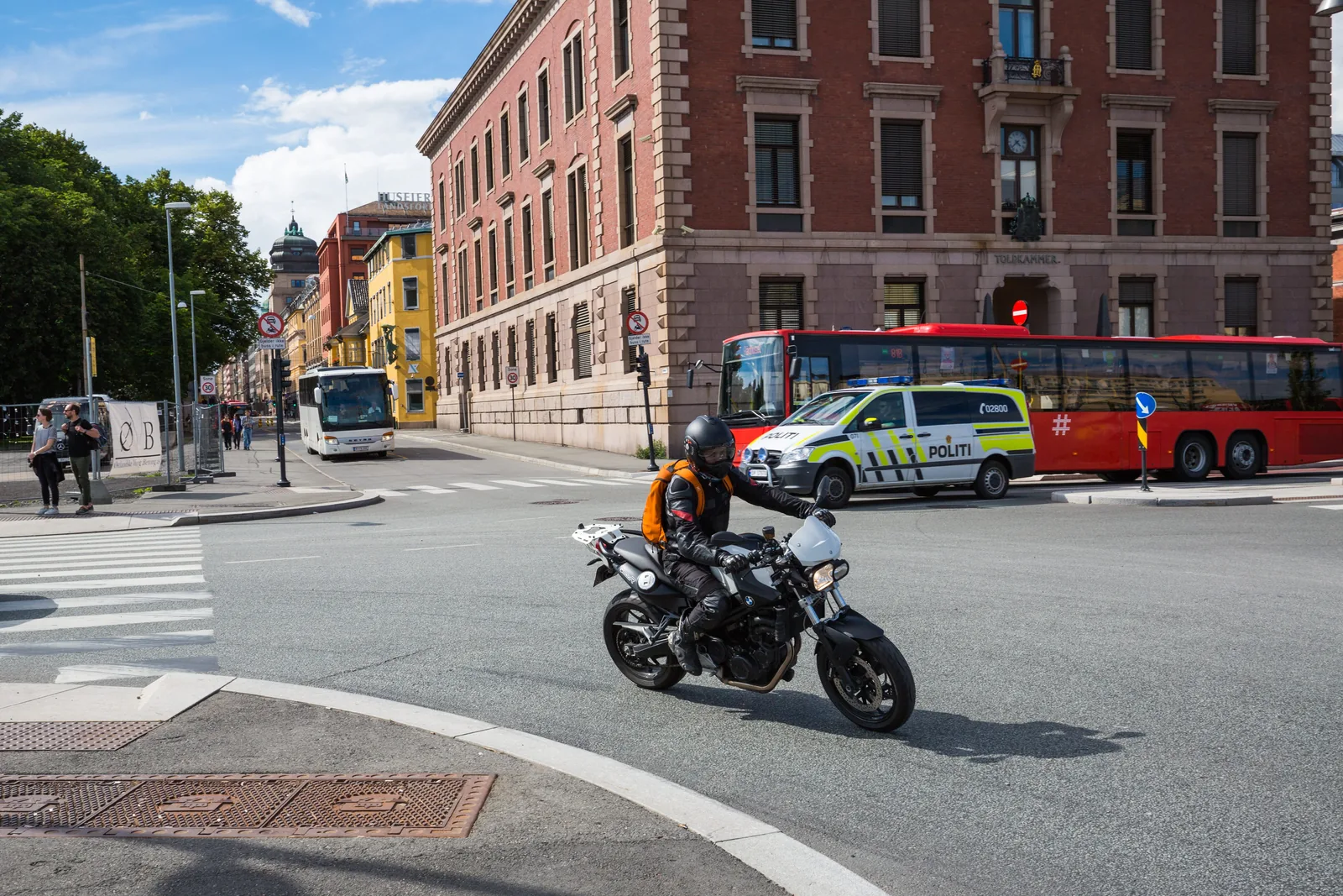 Motorsyklist i et bykryss med buss, politibil og fotgjengere