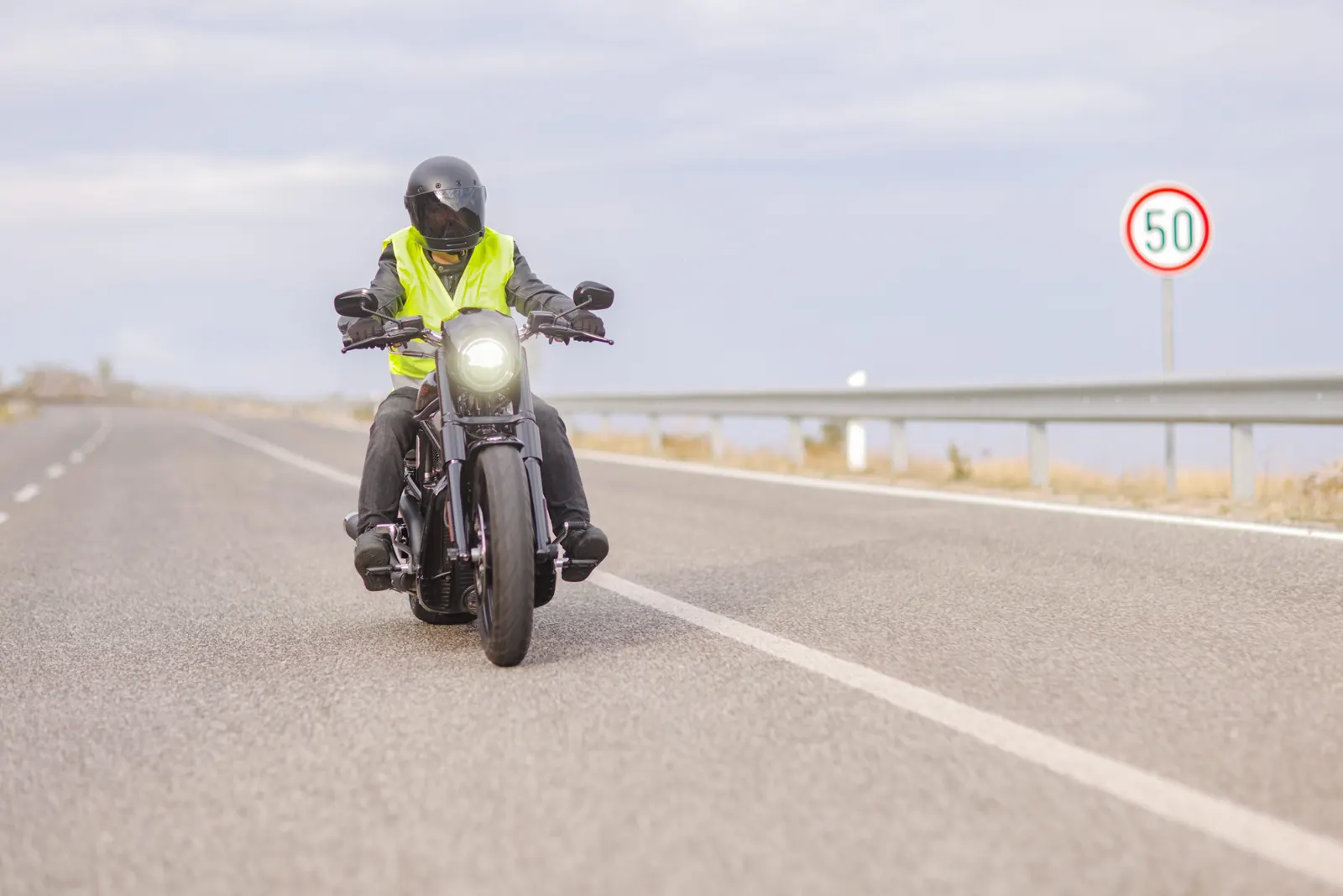 Motorsyklist med hjelm og synlighetsvest kjører på en landevei