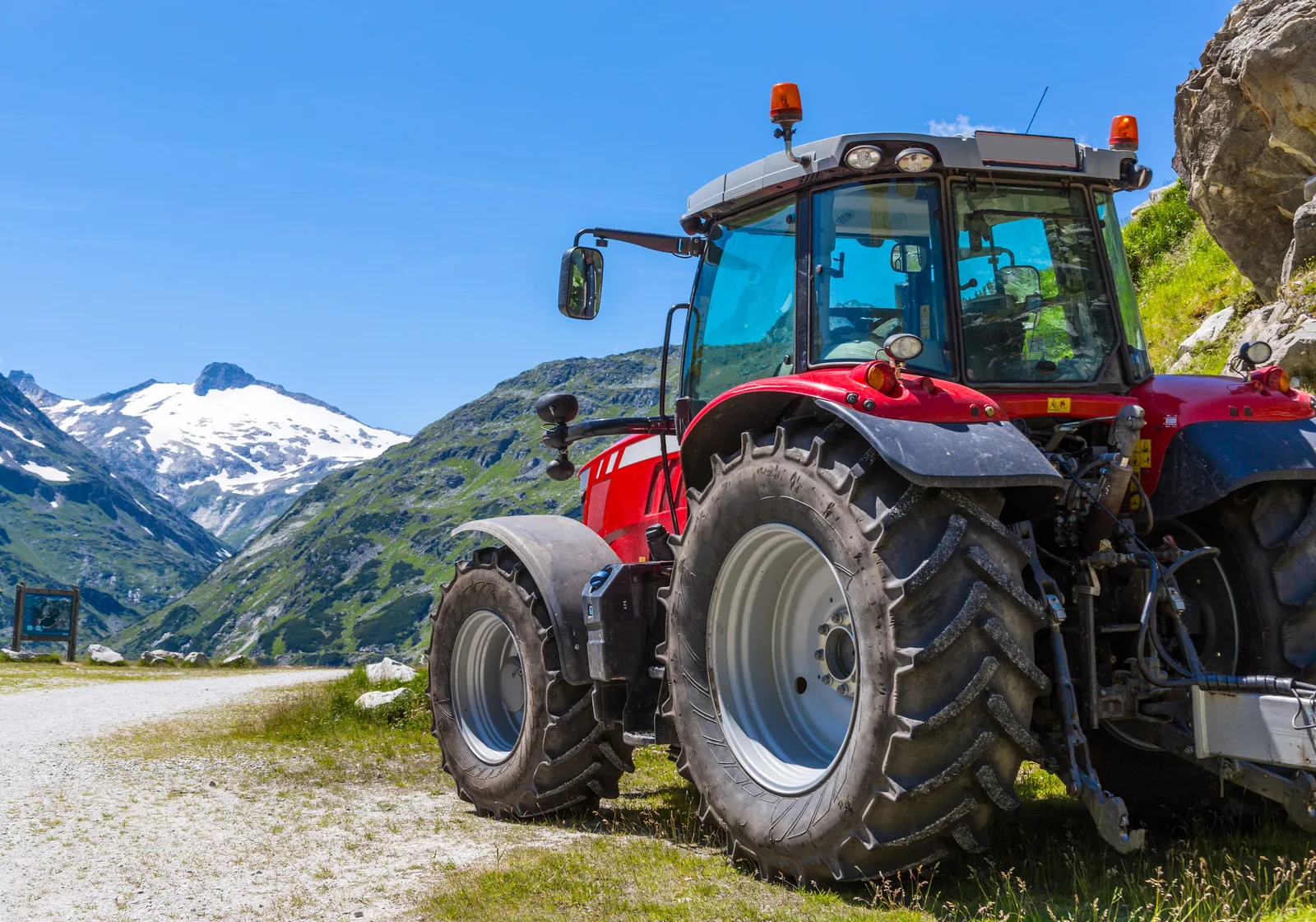 Rød traktor på en fjellvei med snødekte fjell i bakgrunnen